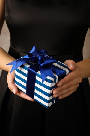 Young woman holding gift box with blue bow, close up