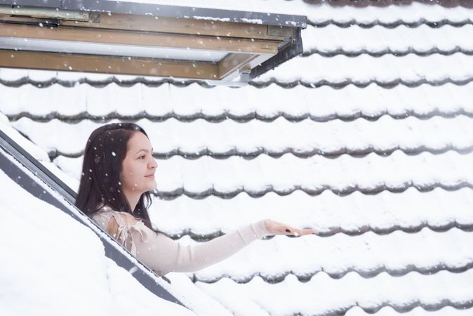 Woman reaching snowflakes through roof window