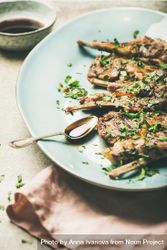 Plate of grilled lamb chops with parsley garnish on light blue plate with copy space 5rPw1b