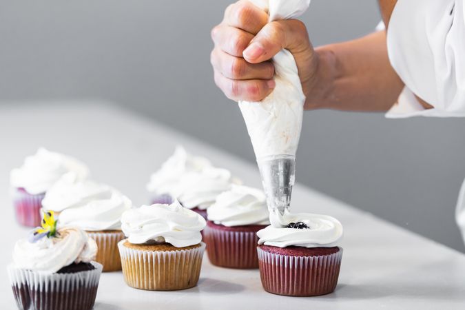 Crop cook decorating cupcakes with whipped cream