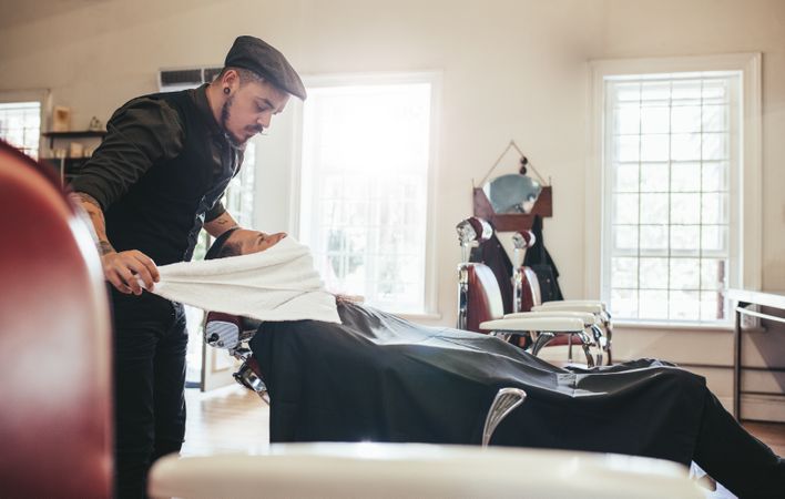 Barber applying towel to customer’s neck in barbershop