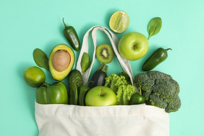 Bag with vegetables and fruits on mint background