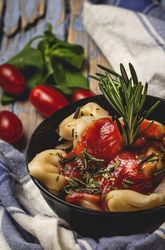 Bowl of delicious ravioli with tomato sauce and rosemary on shabby table