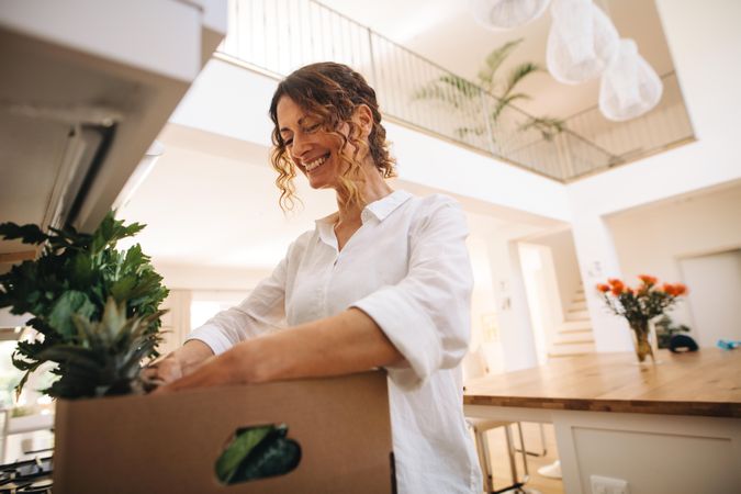 Smiling woman looking in the box of groceries in her kitchen