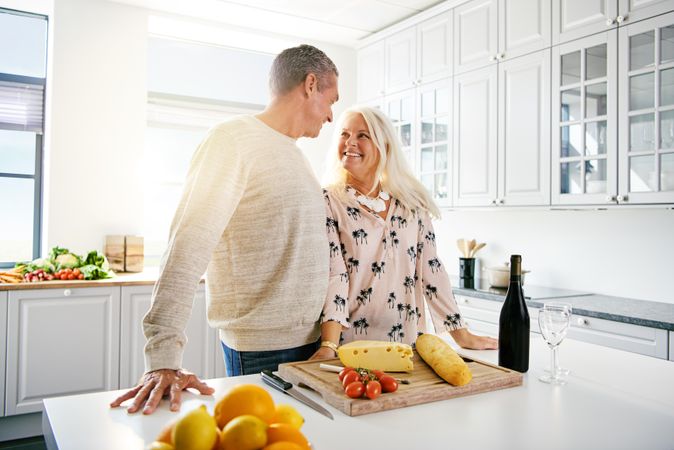 Grey haired couple in front of cutting board with cheese, tomato and baguette