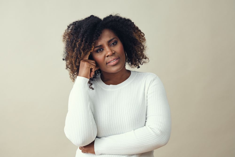 Black woman with her hand to her temple thinking carefully about something