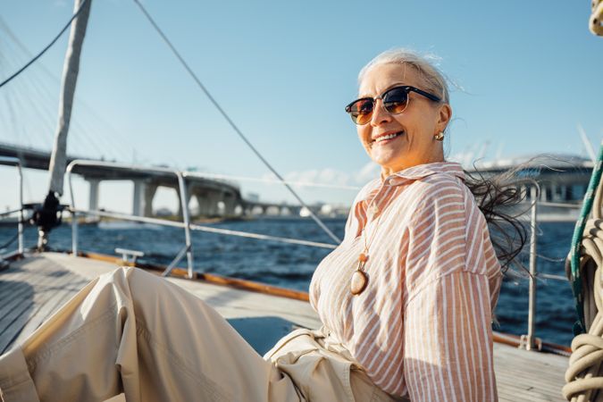 Stylish mature woman sitting on a yacht bow wearing sunglasses