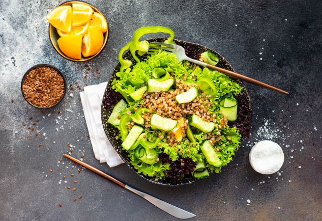 Top view of green fresh salad on concrete background served with flax seed and lemon slices with copy space