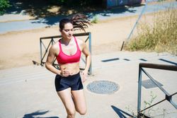 A determined woman jogging upstairs outdoors, showing strength and endurance during a workout on a sunny day