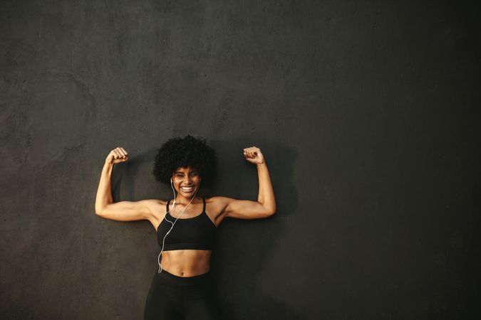 Strong woman flexing muscles and smiling against grey wall