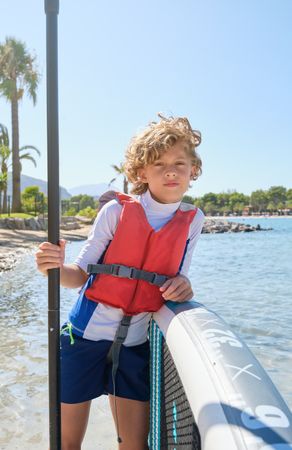 Teenage boy leaning on paddleboard on beach