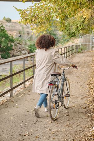 Unrecognizable woman walking with bicycle on road in park
