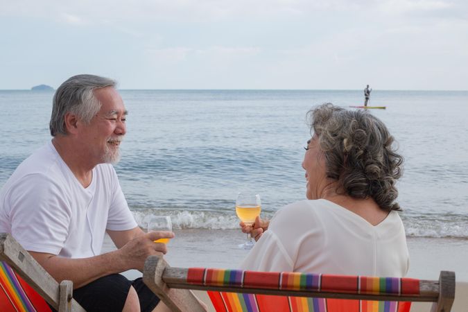 Older Asian couple relaxing on the beach with wine