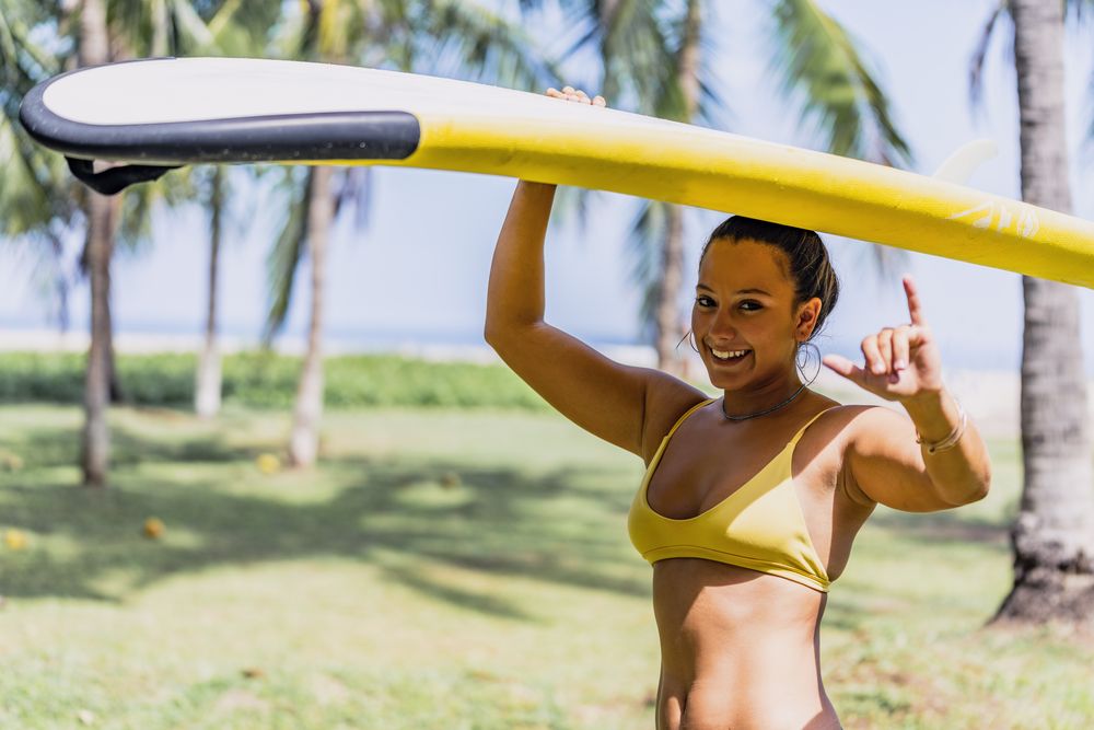 Woman in bikini with bright paddleboard on beach