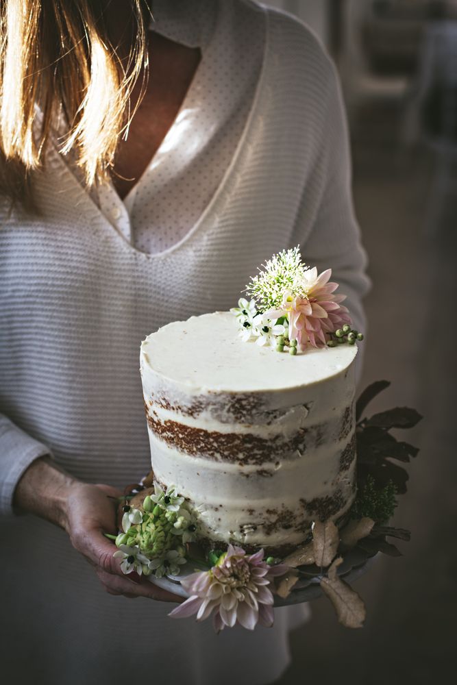 Smiling woman holding plate with cake decorated by flowers and plants