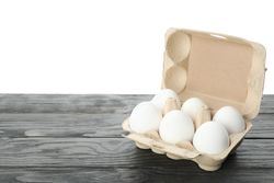 Few raw chicken eggs in carton box on wooden table against light background