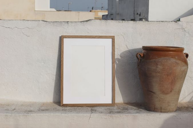Blank vertical wooden frame picture mock up with vintage olive clay storage pot, vase