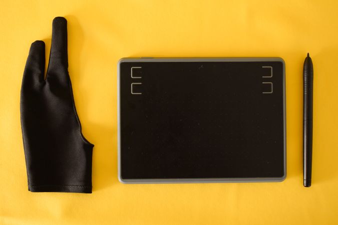 Top view of digital tablet, glove and stylus on yellow table with space for text