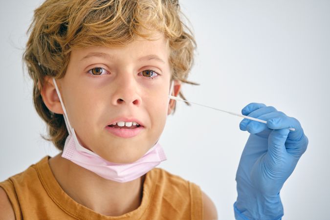 Crop nurse with swab touching face of crying boy