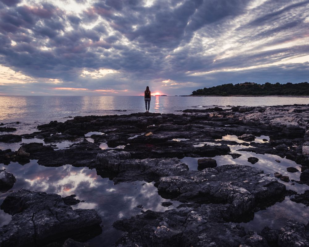 Person standing on rocks facing the ocean