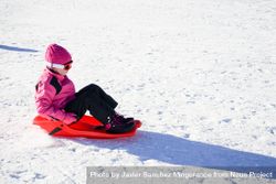 Child in pink snow suit sledding at resort 5RmjD0