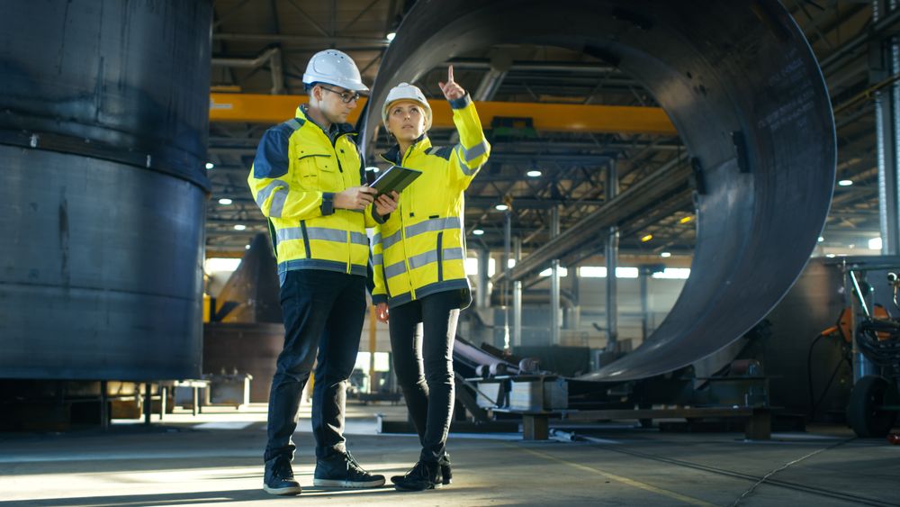Male and Female Industrial Engineers in Hard Hats Discuss New Project while Using Tablet Computer.