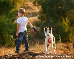 Young boy in jeans with dog on a leash in forest 0JLBZ4
