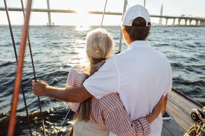 Back view of romantic older couple embracing on a sailboat and enjoying sunset