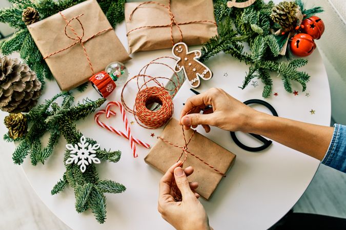 Crop person tying bow on Christmas present on decorated table