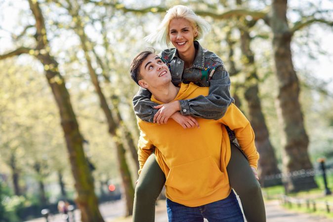Male giving blonde female friend piggy back in park