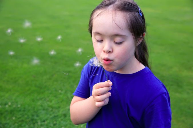 Young child blowing dandelion in a park