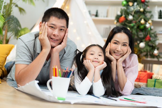 Happy Asian family with chin on hand pose, lying on floor with cozy tent