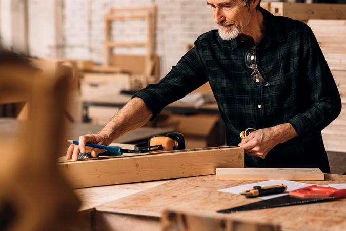 Man measuring piece of wood in his carpentry studio