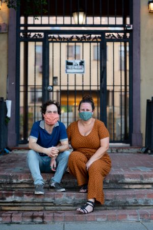 Portrait of loving couple sitting on stoop in front of apartment building with masks