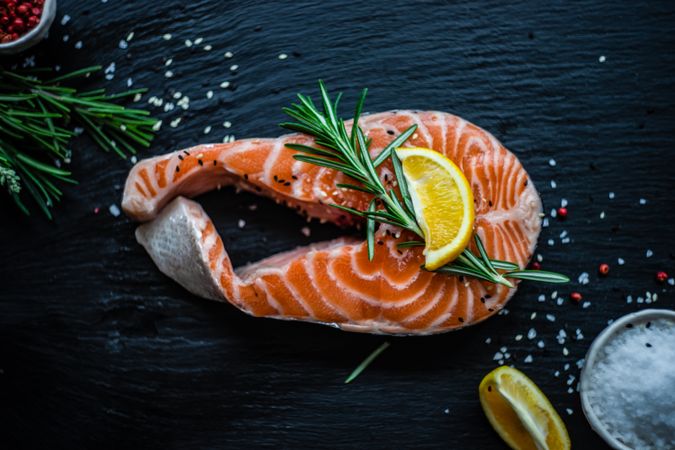 Top view of salmon steak with rosemary and lemon on dark counter with copy space