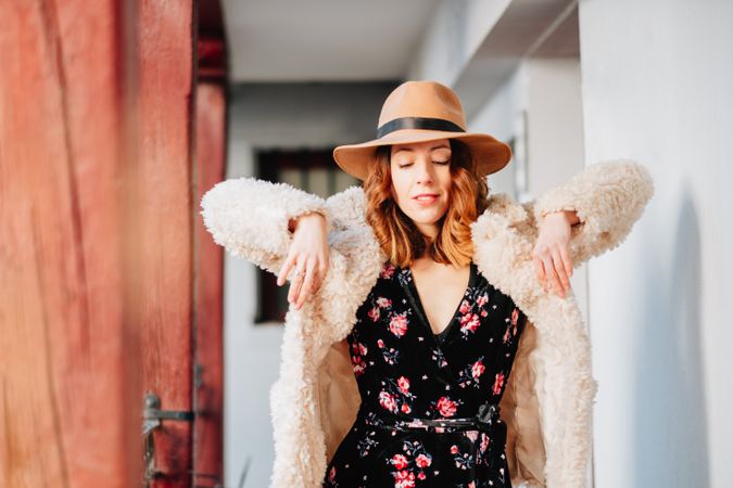 Smiling woman in warm wear standing near building and fence