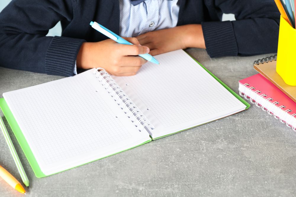 Boy writes in a notebook on grey table, space for text
