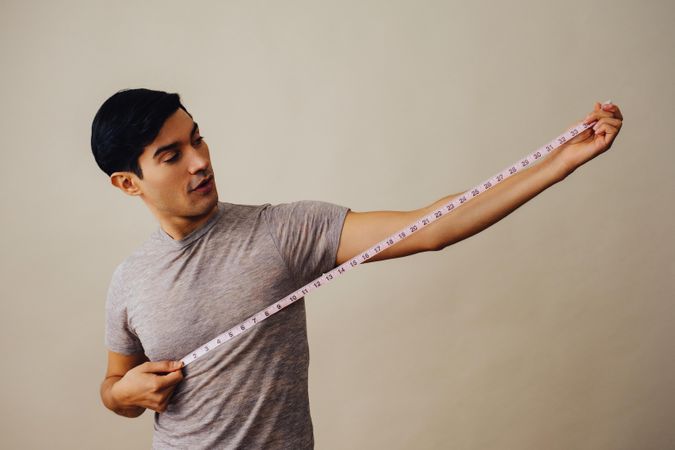 Surprised Hispanic male holding measuring tape out to his side in beige studio shoot