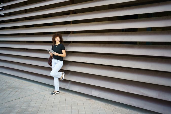 A casual young woman is leaning against a modern architectural wall, radiating confidence and style