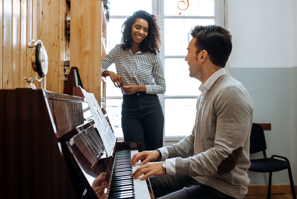 Man playing piano near woman teaching in studio