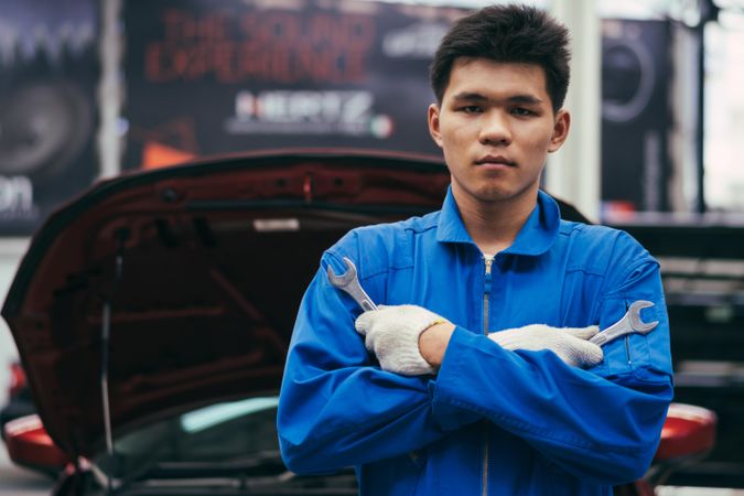 Asian male mechanic holding wrench in front of car