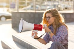 Woman sitting outside with megaphone dressed in checkered shirt