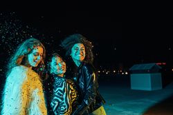 Group of female friends lit in green blue light at night surrounded in confetti