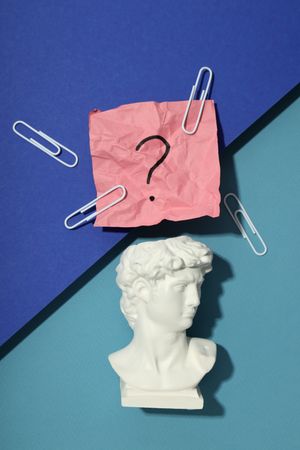 Marble bust of David with crumpled post it note with question mark and paper clips, vertical