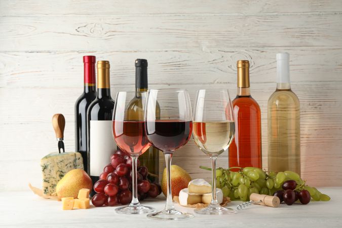 Fruits, cheese, bottles and glasses with different wine on wooden background, space for text