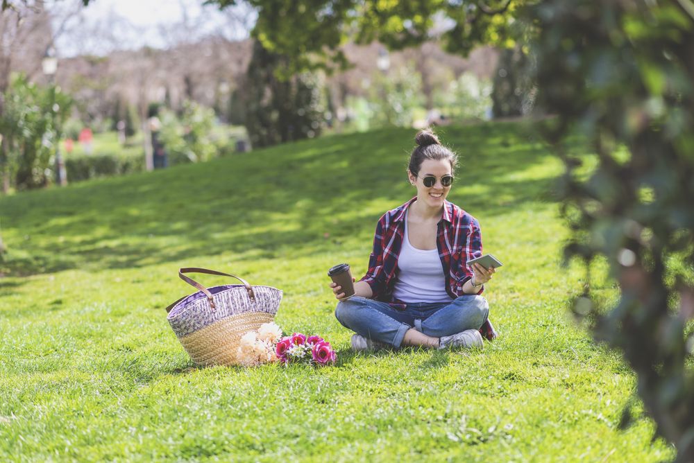 Front view of a young hipster woman sitting on grass in a park