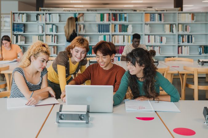 Happy diverse groupmates using laptop and smiling while doing task in library