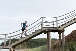 Sportsman running on stairs at shore with mountains