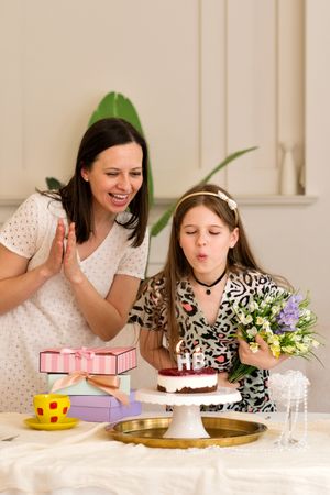 Mother and daughter celebrating birthday, with girl blowing out candles