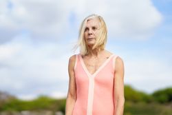 Portrait of stern older woman with  grey hair standing on wooden walkway near the coast